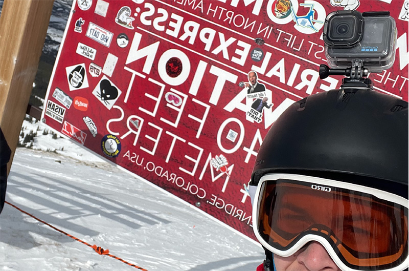 Image of Tyler infront of a trail sign snowboarding